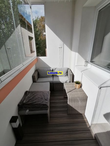 Ein verglaster Balkon mit Rattanmöbeln und einem Boden in Holzoptik in einer Einzimmerwohnung.