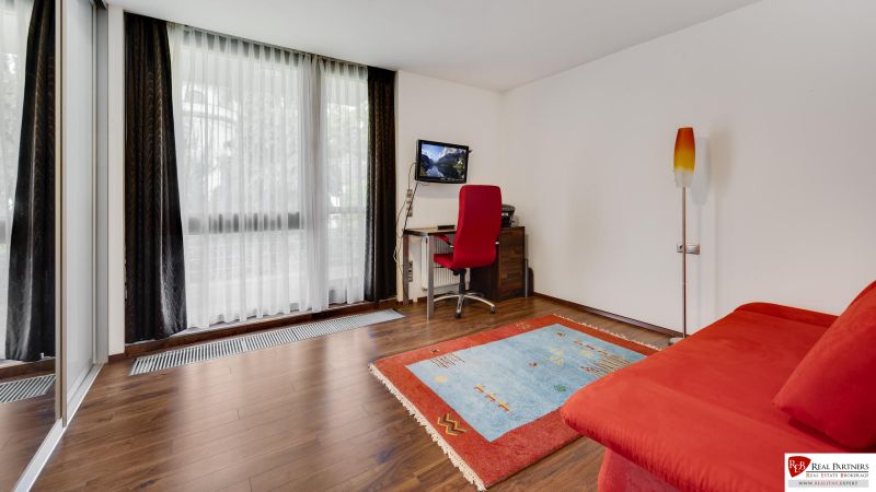 Helles Zimmer mit rotem Sofa, Teppich und Holzboden.