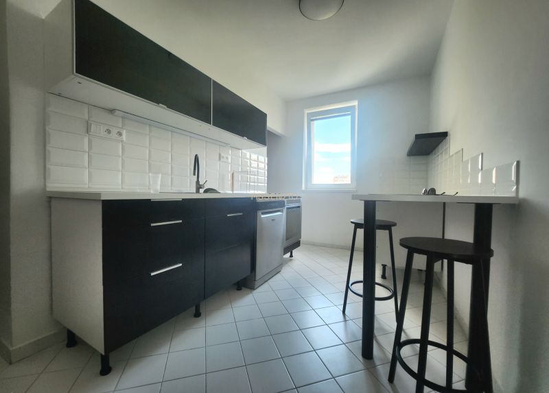 Küche in einer 3-Zimmer-Wohnung mit weißen Fliesen und dunklen Schränken.