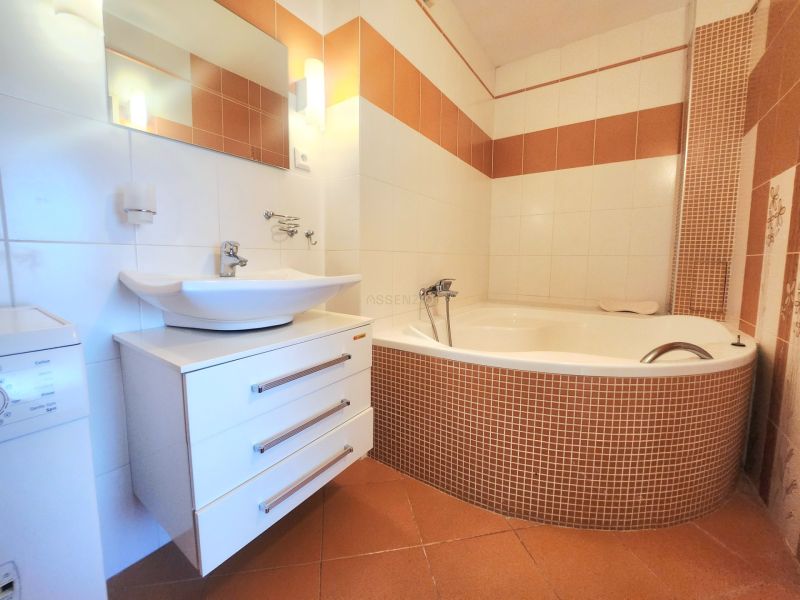 Badezimmer mit einer Eckbadewanne, einem Waschbecken und einer Waschmaschine in einer 3-Zimmer-Wohnung.