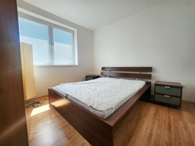 Ein Schlafzimmer mit Sonnenlicht, einem Bett, einem Nachttisch und einem Boden mit Holzdekor.