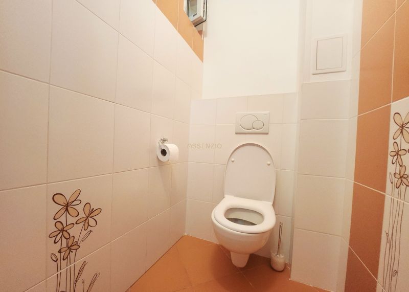Toilette mit weißen Fliesen und orangefarbenen Bodenfliesen in einer 3-Zimmer-Wohnung.