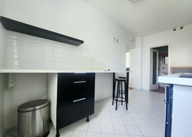 Küche mit weißen Fliesen, schwarzen Möbeln und Barhocker in einer 3-Zimmer-Wohnung.