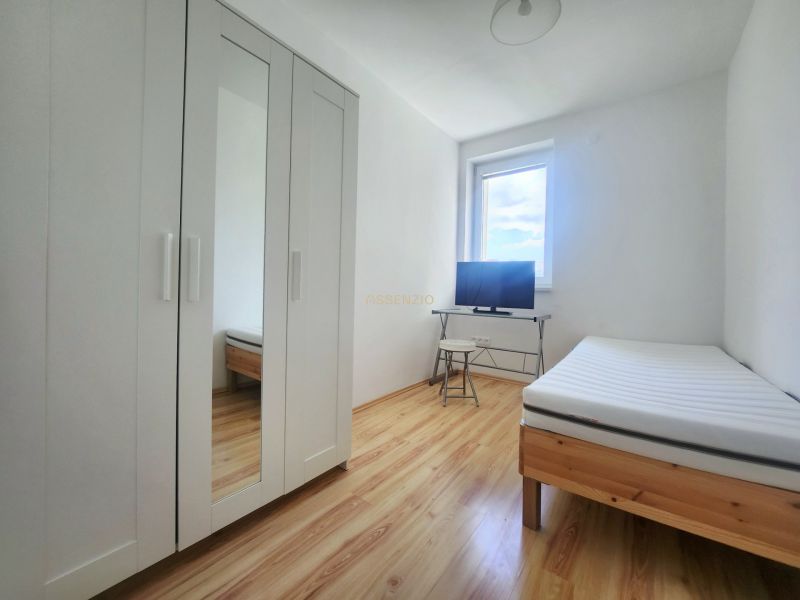 Helles Zimmer mit Bett, weißem Schrank und Fernseher, 3-Zimmer-Wohnung, Boden mit Holzdekor.