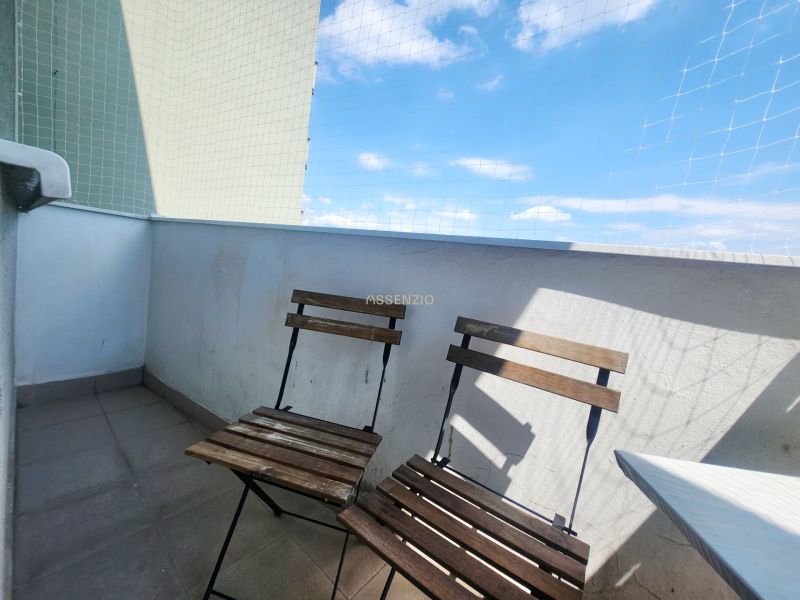 Balkon einer 3-Zimmer-Wohnung mit zwei Holzstühlen, blauem Himmel und Schutznetz.