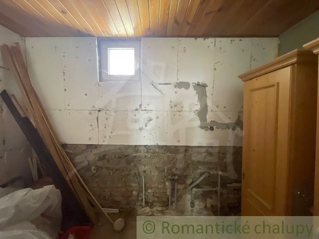 Ein Raum mit einer Holzdecke, einer gemauerten Wand und alten Möbeln in einem Einfamilienhaus.