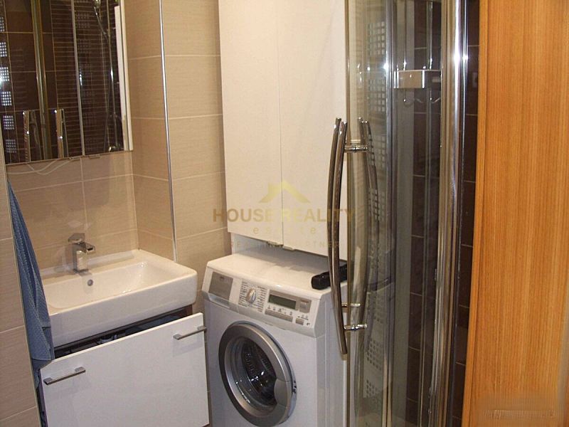 Badezimmer mit Waschmaschine in der Ecke neben dem Waschbecken und der Duschkabine in einer Zweizimmerwohnung.