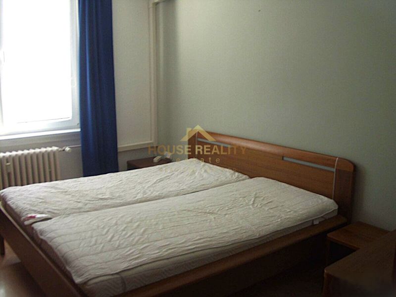 Schlafzimmer in einer 2-Zimmer-Wohnung mit Ehebett, Fenster und Vorhang.