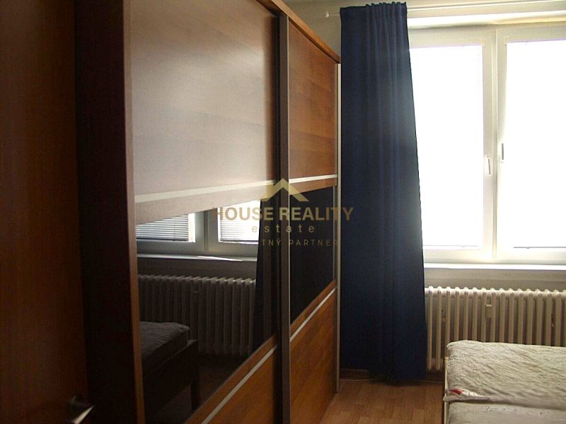 Ein Schrank mit Schiebetüren, ein Bett und ein Heizkörper im Schlafzimmer einer Zweizimmerwohnung.