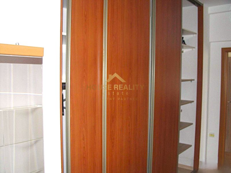Einbauschrank mit Holzdekor in einer 2-Zimmer-Wohnung, ergänzt durch weiße Wände und Regale.