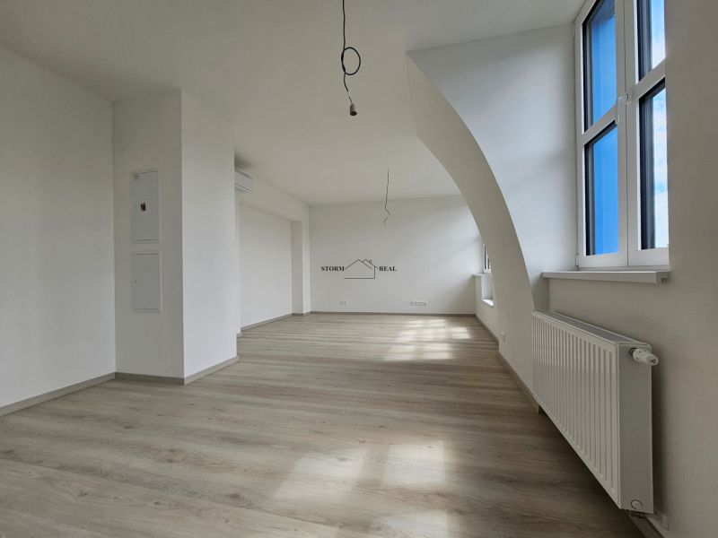 Geräumiges Wohnzimmer mit Holzboden und großen Fenstern in einer Einzimmerwohnung.
