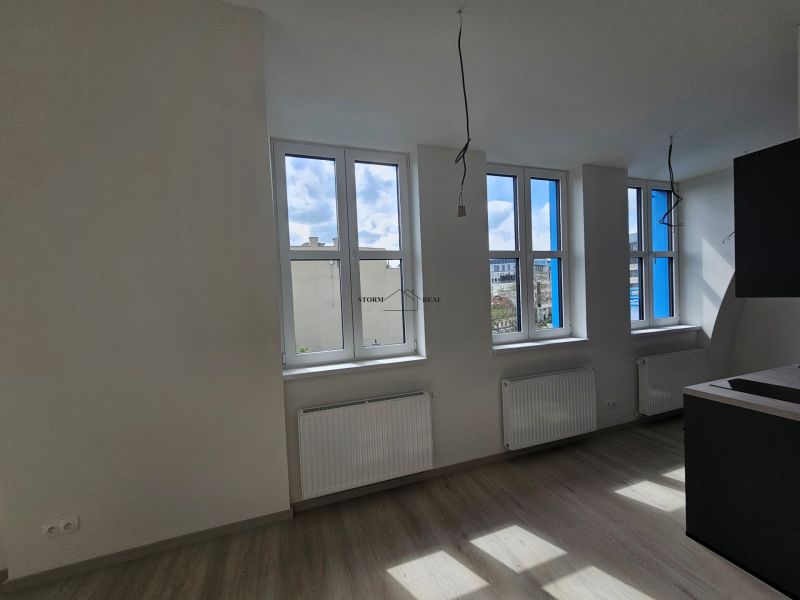 Helles Zimmer mit drei Fenstern und Holzboden in einer Einzimmerwohnung.
