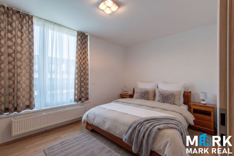 Schlafzimmer mit großem Fenster, Doppelbett und Holzboden in einer Zweizimmerwohnung.