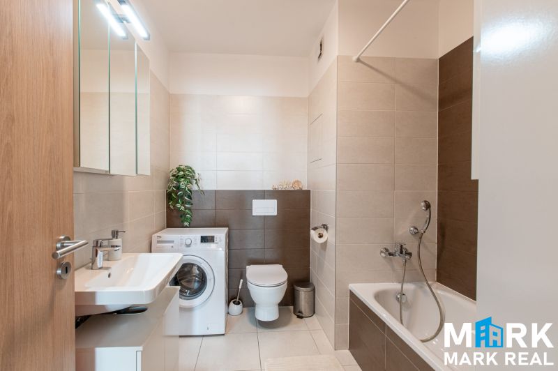 Badezimmer mit Badewanne, Waschmaschine und Waschbecken in einer 2-Zimmer-Wohnung.