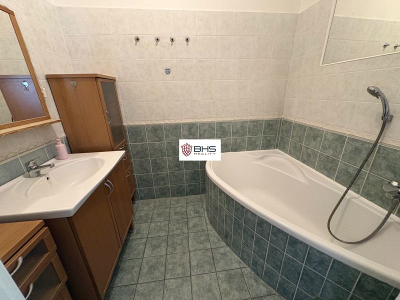 Badezimmer mit Badewanne, Waschbecken und Schrank in einer 2-Zimmer-Wohnung, Fliesen und Wandverkleidungen.