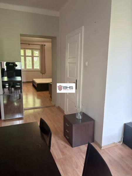 Innenraum einer 2-Zimmer-Wohnung mit Holzboden, Sitzbereich und Eingang zum Schlafzimmer.
