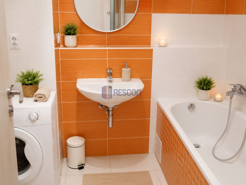 Badezimmer in einem Studio-Apartment mit orangefarbenen Fliesen, Waschbecken und Badewanne, Pflanzen zur Dekoration.