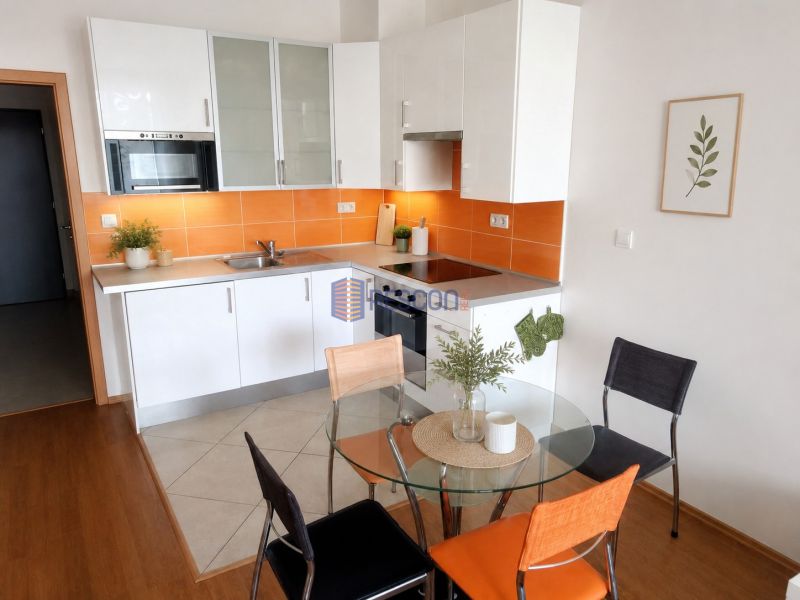 Eine Küche in einem Einzimmerapartment mit weißer Küchenzeile, orangefarbenen Fliesen und einem runden Tisch mit Holzdekor.