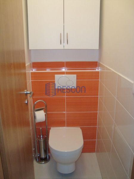 Toilette mit orangefarbenen Fliesen und weißem Schrank, Einzimmerwohnung.