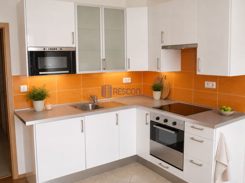 Eine Küche mit weißen Schränken, eingebautem Ofen und orangefarbenen Fliesen in einem Einzimmerapartment.