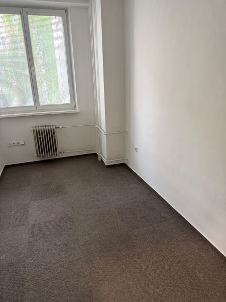 Büro mit Teppichboden, Heizkörper und Fenster mit Jalousien.