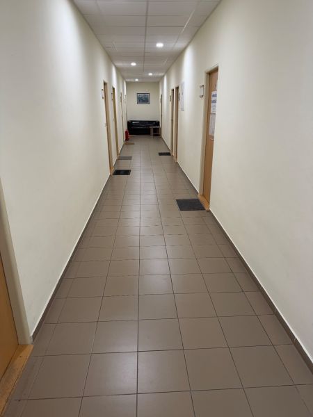 Ein enger Flur in einem Büro mit Fliesen, Türen und einem Sofa am Ende.