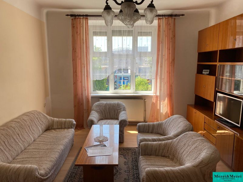 Wohnzimmer in einer Zweizimmerwohnung mit Sofa, Sesseln, Fernseher und Möbeln.
