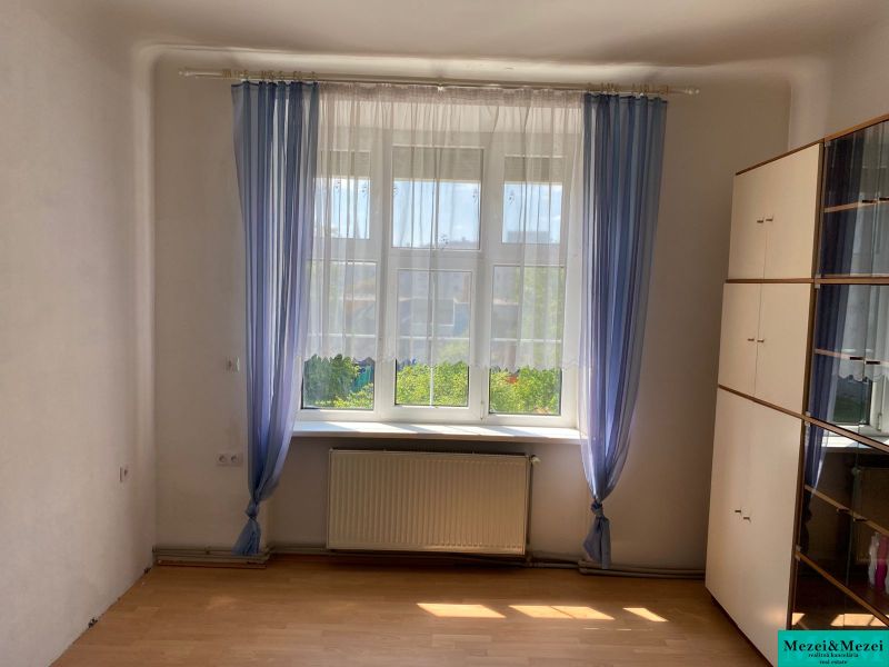 Ein Zimmer mit einem Schrank, Fenster und Vorhängen in einer 2-Zimmer-Wohnung, Boden mit Holzdekor.