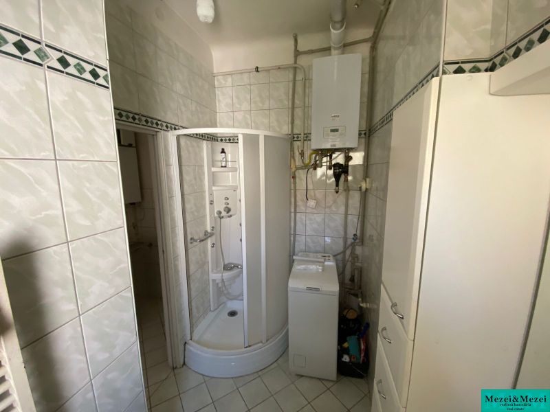Badezimmer mit einer in der Ecke platzierten Duschkabine und einer Waschmaschine in einer 2-Zimmer-Wohnung.
