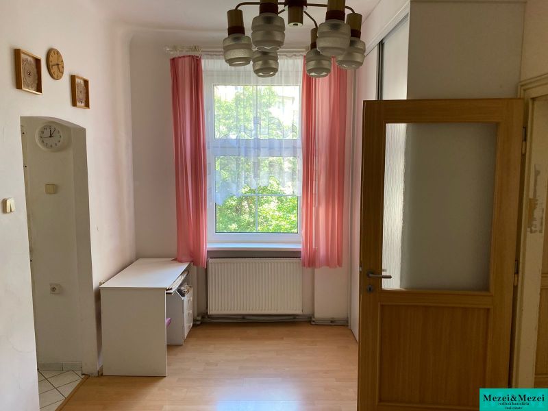 Ein Zimmer mit Holzboden und rosa Vorhängen in einer Zweizimmerwohnung.