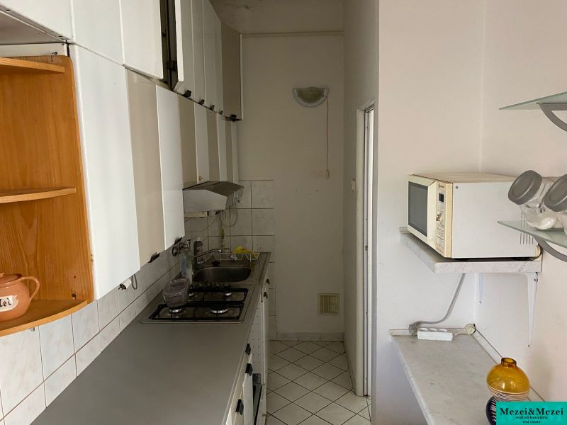 Eine schmale Küche in einer Zweizimmerwohnung mit weißen Möbeln und Fliesen.