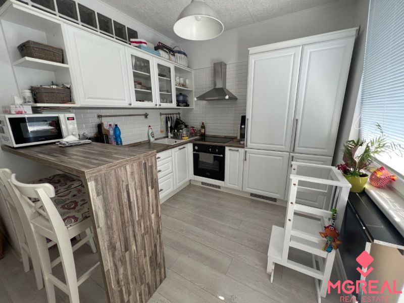 Küche in einer 2-Zimmer-Wohnung mit weißen Möbeln, Bartresen und Boden in Holzoptik.
