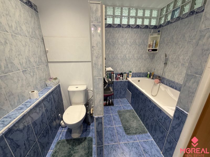Badezimmer in einer 2-Zimmer-Wohnung mit Badewanne und blauen Fliesen.