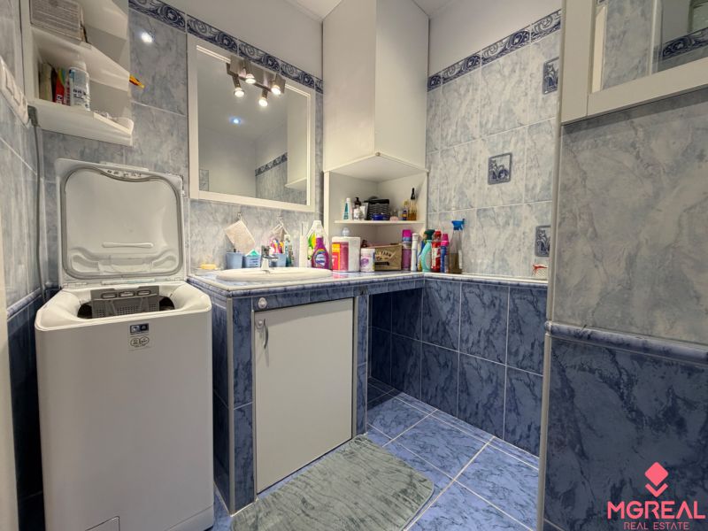 Badezimmer in einer 2-Zimmer-Wohnung mit Waschmaschine und blauen Fliesen.