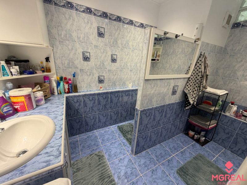 Badezimmer mit blauen Fliesen und einem Regal in einer Zweizimmerwohnung mit Toilettenartikeln.