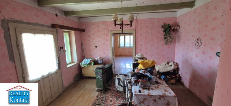 Ein Zimmer in einem Einfamilienhaus mit älteren Möbeln, rosa Tapeten und Holzboden.