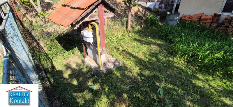 Der Garten des Einfamilienhauses in Dedinka mit Rasen, Gaszähler und einem Erdhaufen im Hintergrund.