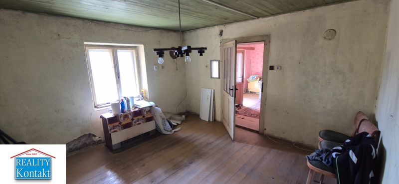 Ein Zimmer in einem Einfamilienhaus mit einem Holzboden, älteren Möbeln und einem Fenster.