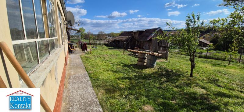 Ein Einfamilienhaus in Dedinka mit einem großen Garten, viel Grün und einem älteren Gebäude im Hintergrund.