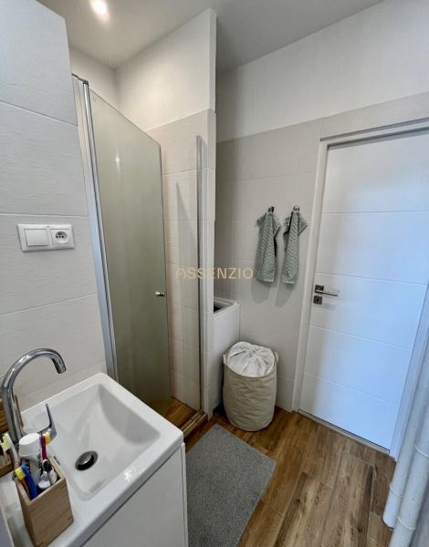 Badezimmer in einer 2-Zimmer-Wohnung mit Holzboden, Duschkabine und Waschmaschine.