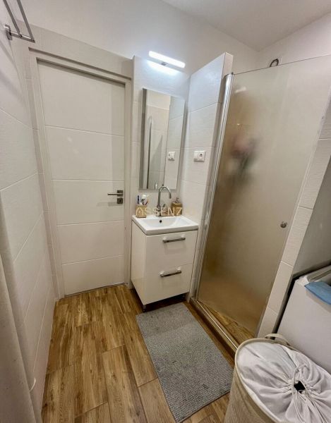 Badezimmer in einer 2-Zimmer-Wohnung mit Holzdekorboden, Duschkabine und Waschbecken.