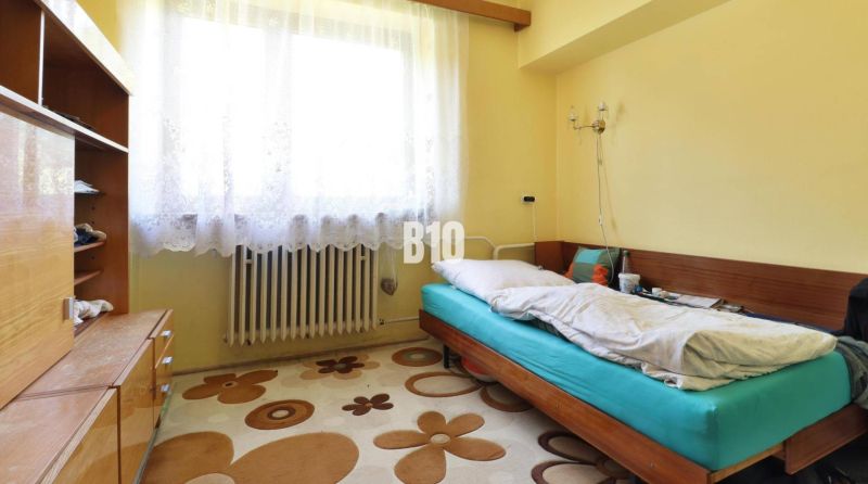 Ein Zimmer in einem Einfamilienhaus mit einem Einzelbett, einem Schrank und einem Fenster mit weißen Vorhängen.