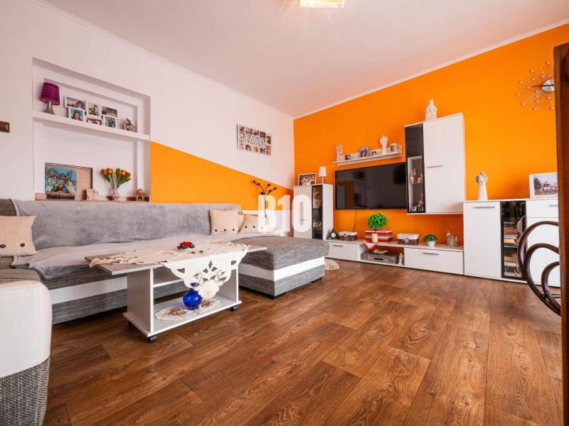 Wohnzimmer mit orangefarbener Wand, Sofa und Holzboden in einem Einfamilienhaus.
