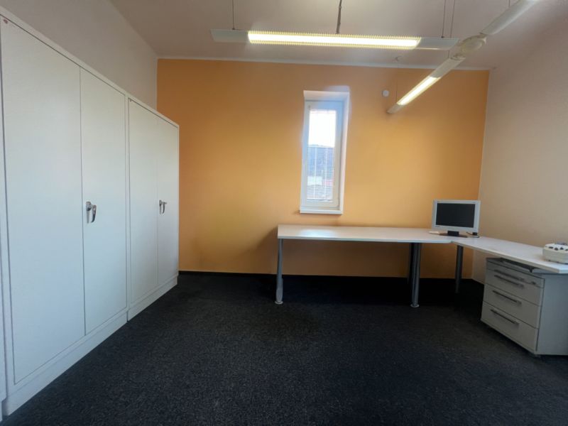 Ein Büro mit Möbeln, einem Computer und Schränken auf einem hellen Boden.