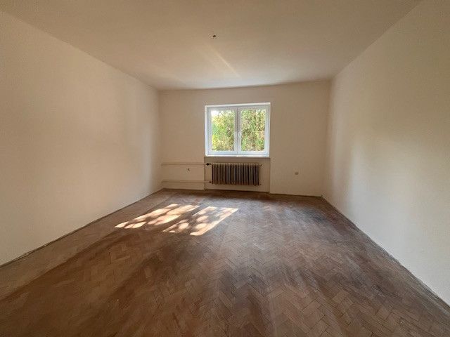 Ein geräumiges Zimmer in einem Einfamilienhaus mit einem Holzboden und einem großen Fenster.