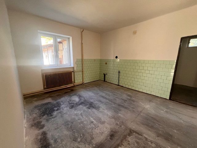 Ein Zimmer in einem Einfamilienhaus mit einem Fenster, einem Heizkörper und hellgrünen Fliesen.