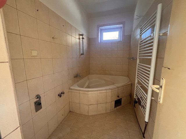Ein Badezimmer in einem Einfamilienhaus mit einer Eckbadewanne und einem Heizkörper an der Wand.