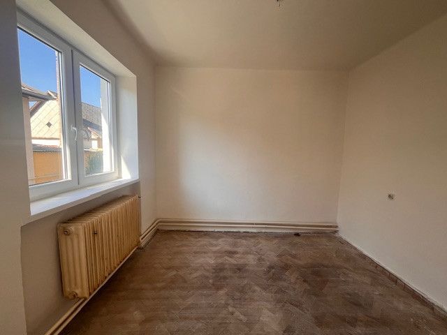 Ein Zimmer in einem Einfamilienhaus mit einem Fenster und einem Boden in Holzoptik.
