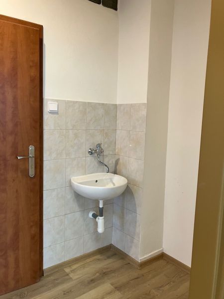 Kleines Waschbecken mit Fliesen und Boden in Holzoptik im Büro.