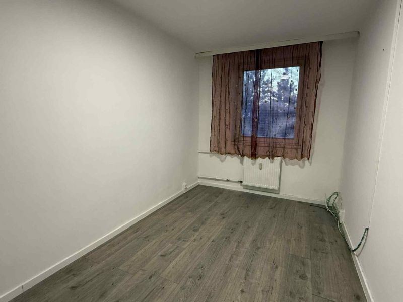 Ein Zimmer in einer 4-Zimmer-Wohnung mit einem Boden in Holzoptik und einem einfachen Vorhang.